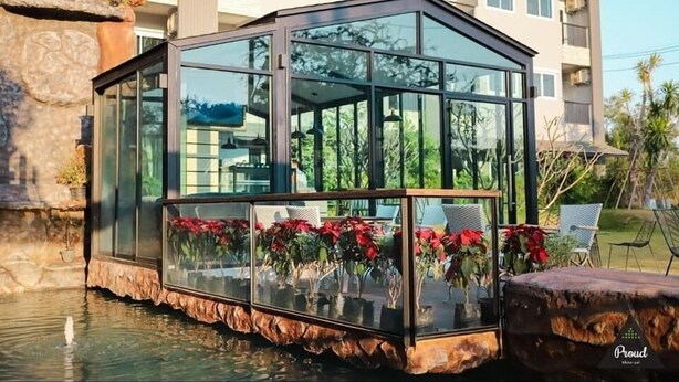 A glass-enclosed structure with a stone base, surrounded by water and potted plants. - Proud Khaoyai (Pak Chong)