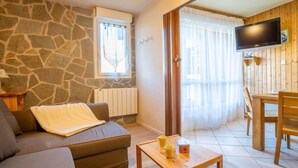 Ein gemütliches Wohnzimmer mit Steinwand, einer Couch, einem Couchtisch mit Tassen und einem an der Wand montierten Fernseher.