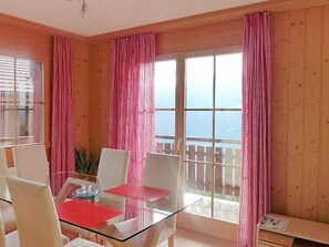 A room with a glass table, white chairs, a red tablecloth, and a view of the sea through large windows with red curtains. - Berg-Seeblick by Interhome (Beatenberg)