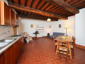 Una cucina funzionale con mobili in legno, una zona pranzo con tavolo e sedie, e un angolo salotto accogliente con divano e lampada.