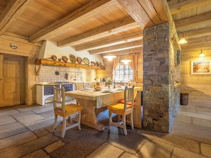 Una cocina rústica con vigas de madera, un pilar de piedra y un comedor con sillas de madera.