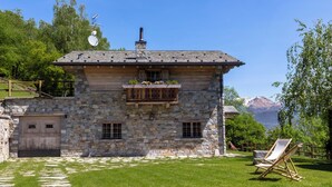 Una casa in pietra con un balcone, un pontile in legno e vista sulle montagne.