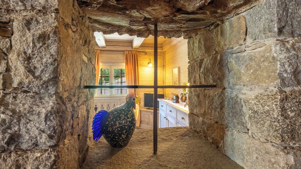 Un interno rustico con pareti in pietra, soffitto in legno e un gallo appeso.