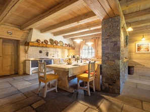 Una cocina rústica con vigas de madera, una columna de piedra, un salpicadero de azulejos y un comedor con sillas y una mesa de madera.