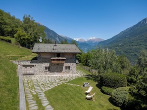 Una casa de piedra con balcón, un sendero de piedra y un jardín con dos sillones de descanso.