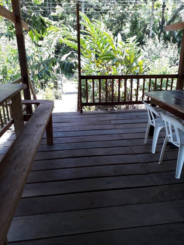 A wooden deck with a table and chairs, surrounded by lush greenery. - Cabaña Los Termales (Nuquí)
