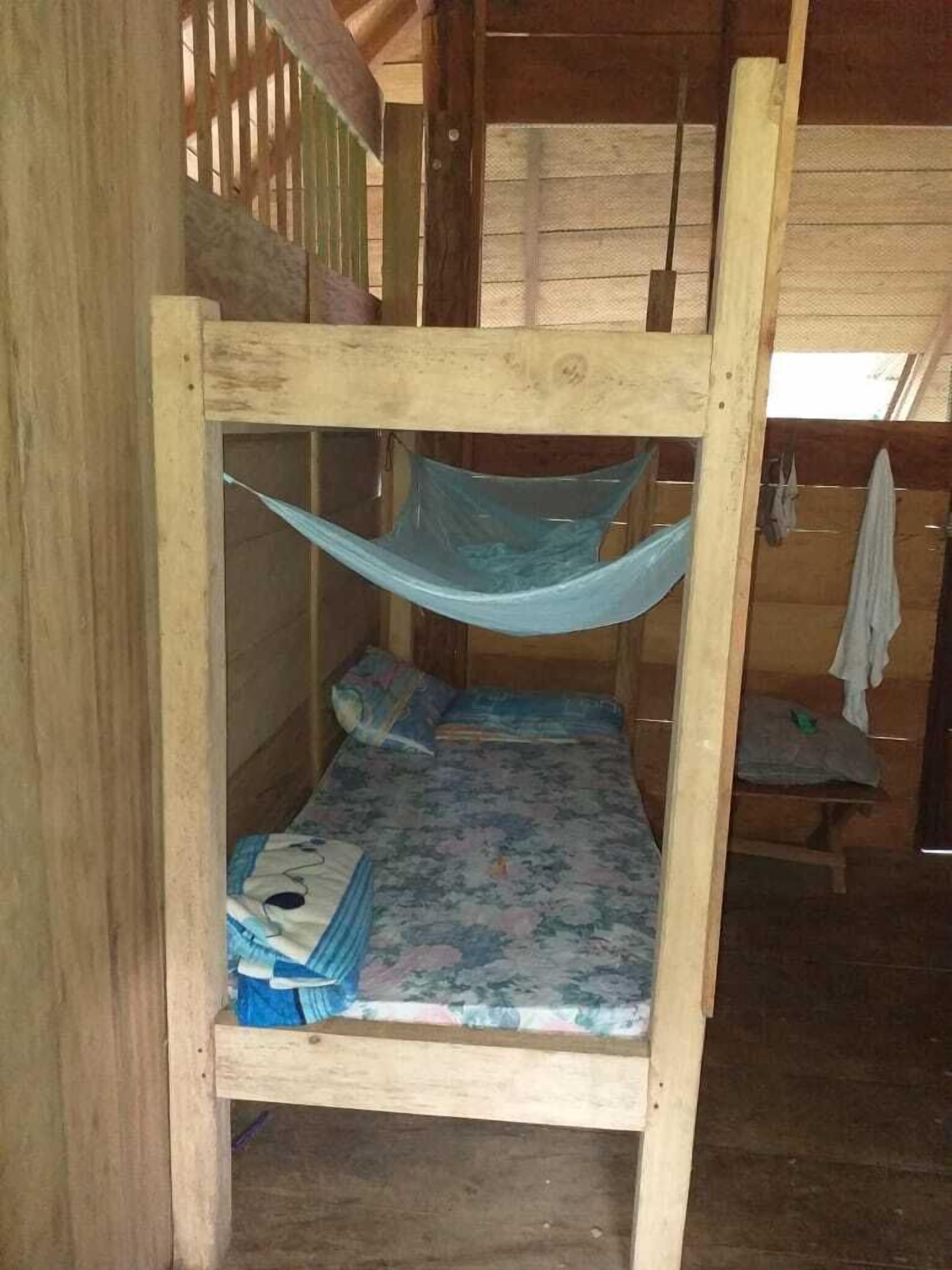 A single wooden bunk bed with a blue net, a floral bedspread, and a small table with a pillow.