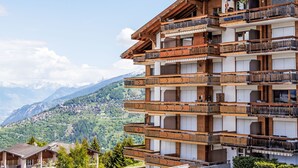 A multi-story wooden building with balconies, set against a mountainous backdrop. - Victoria 1 C1 by Interhome (Nendaz)