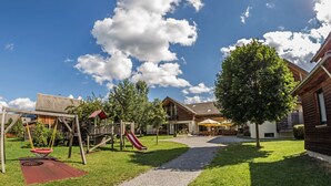 Ein Spielplatz mit Schaukeln und Rutschen, einer überdachten Sitzgelegenheit und einem Kiesweg.