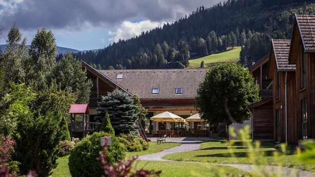 Eine Holzhütte mit Außenbestuhlung und Blick auf eine gebirgige Landschaft.