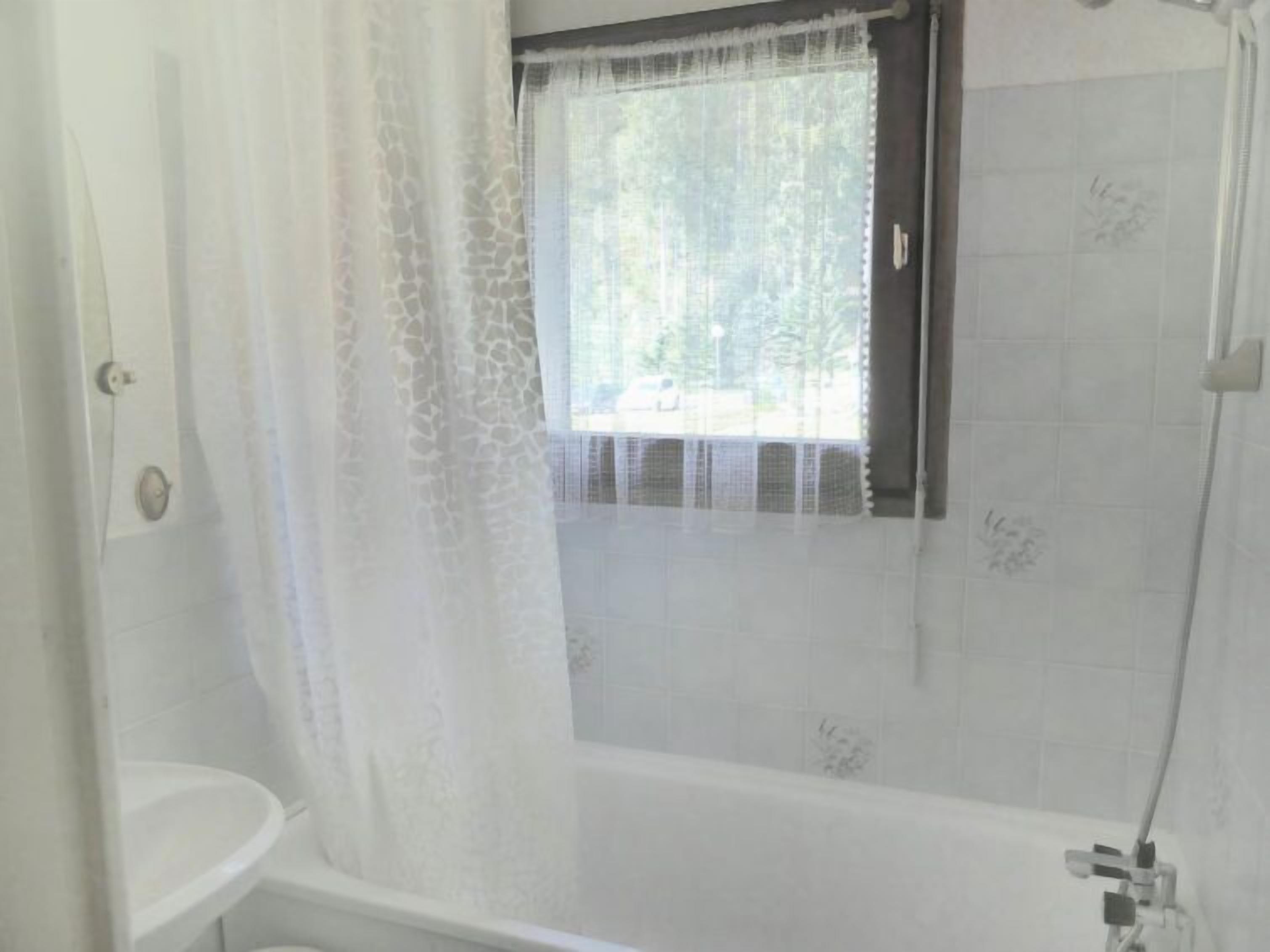 A bathroom with a bathtub, a toilet, and a window with a curtain.