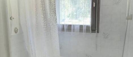 A bathroom with a bathtub, a toilet, and a window with a curtain.