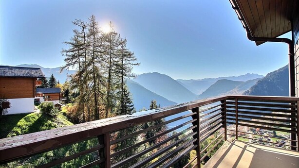 A balcony with a view of mountains and a tree.