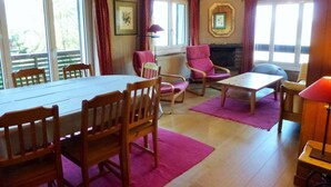 A room with a dining table, chairs, a fireplace, and large windows.