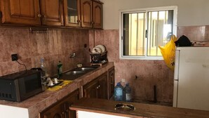 Une cuisine avec des meubles de rangement en bois, un four à micro-ondes, un évier et une fenêtre avec des stores.