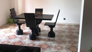 Un coin repas avec une table et des chaises noires, un tableau encadré au mur et des carreaux de sol à motifs.