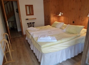 Ein Schlafzimmer mit Holzboden, einem Bett mit weißer Bettwäsche, einem Holzkopfende, einem Nachttisch und einem an der Wand befestigten Spiegel.