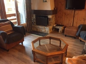 Uma sala de estar aconchegante com lareira de pedra, móveis de madeira e uma televisão de tela plana na parede.