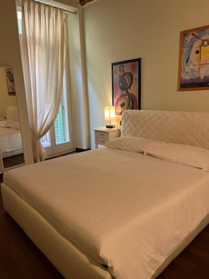A hotel room with a large bed, a bedside table with a lamp, a window with curtains, and a painting on the wall. - Dimora 4 Spade (Verona)
