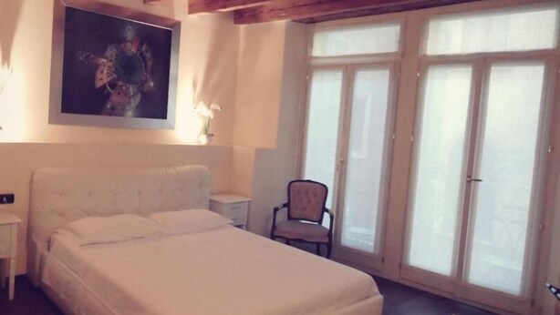 A bedroom with a large bed, a chair, a desk, and a window with blinds. - Dimora 4 Spade (Verona)