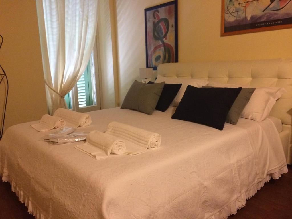 A neatly made bed with white linens and pillows, a painting on the wall, and a window with curtains.