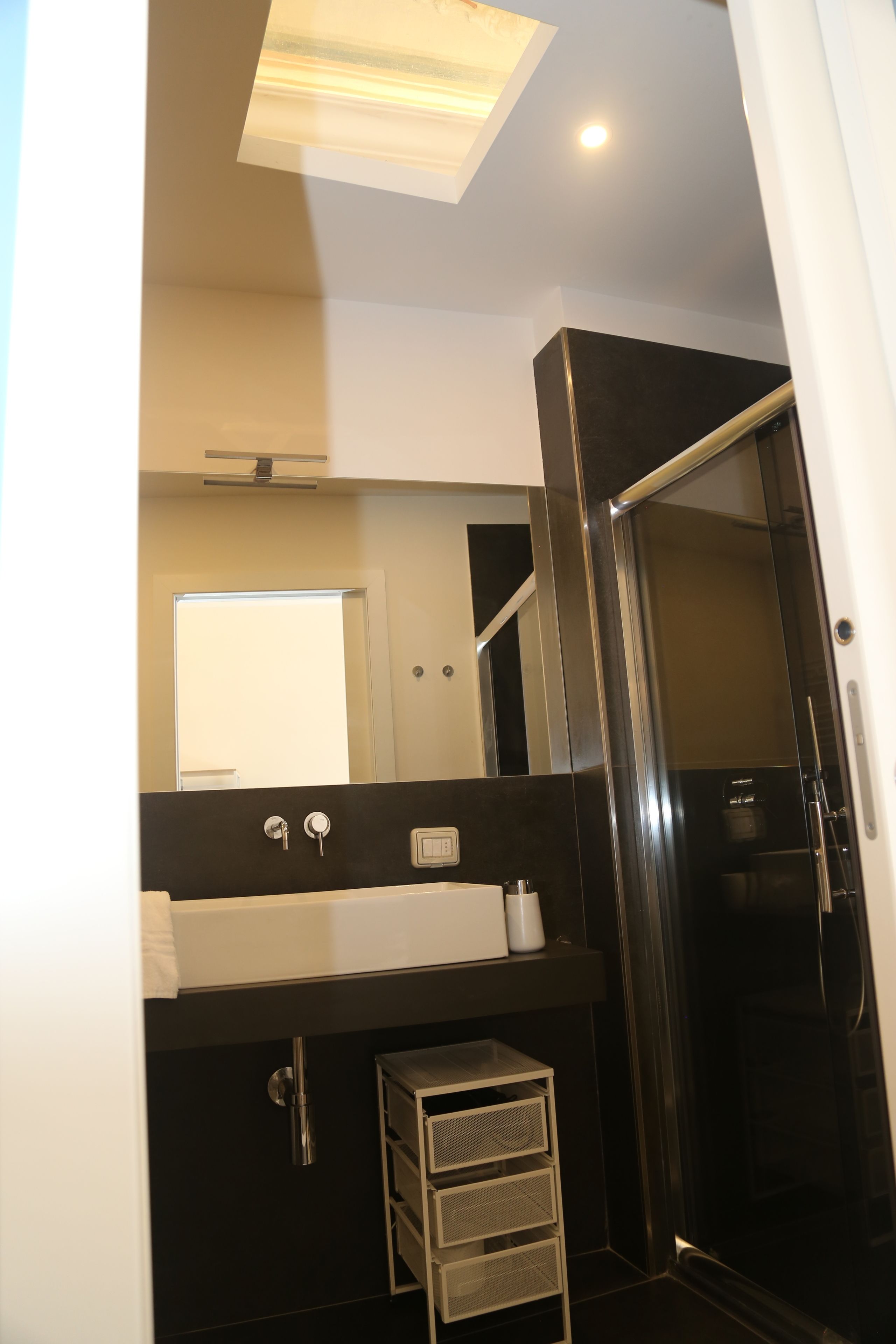 Ein modernes Badezimmer mit Duschkabine aus Glas, einem weißen Waschbecken mit Spiegel darüber und einem kleinen Schrank darunter.