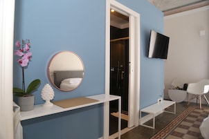 A room with a blue wall, a white console table with a mirror, a potted plant, and a television mounted on the wall.