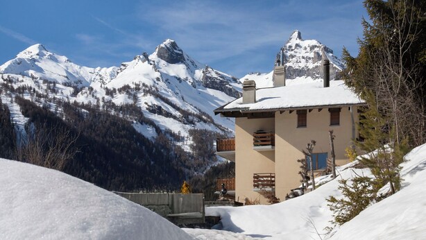 A mountain lodge with a snow-covered roof, wooden balconies, and a view of snow-capped peaks. - Tourbillon A 31 by Interhome (Ovronnaz)