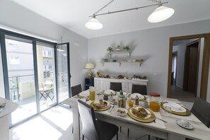 A dining area with a table set for breakfast, a balcony with a chair, and a kitchen area with shelves above the counter. - B&B Malò Family Friendly (Syracuse)