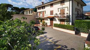 A two-story building with a balcony, a small garden area, and a paved driveway.