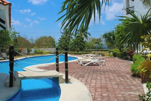 A pool area with a rope bridge, lounge chairs, and palm trees. - Villas Mayaluum Cozumel (Cozumel)