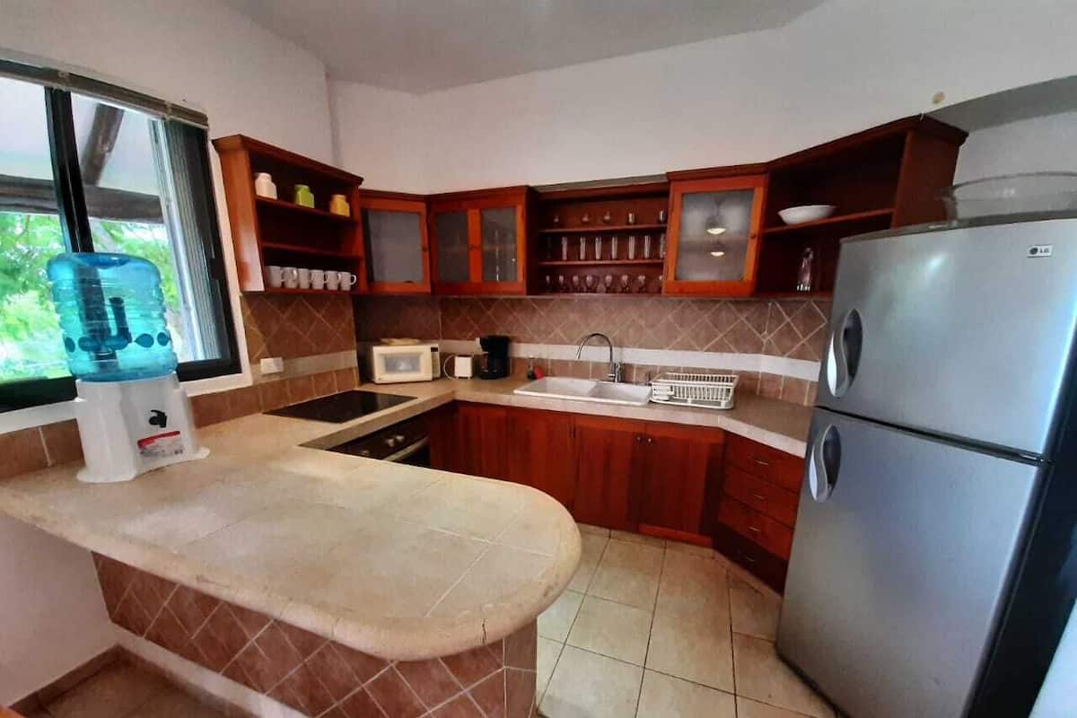 Cozinha com armários de madeira, geladeira de aço inoxidável, micro-ondas e purificador de água.