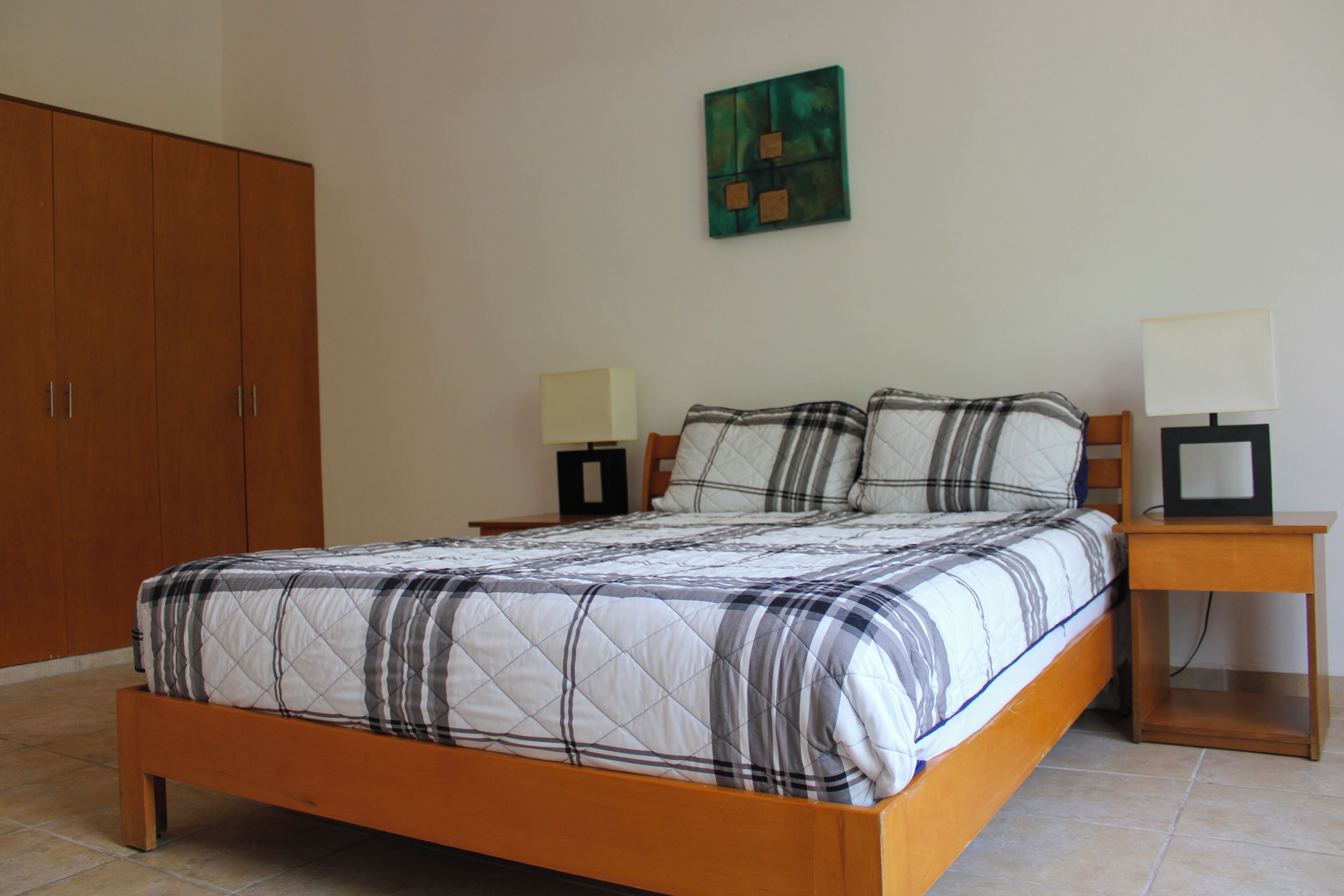 A bedroom with a wooden bed, two bedside tables with lamps, a wardrobe, and a painting on the wall.