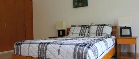A bedroom with a wooden bed, two bedside tables with lamps, a wardrobe, and a painting on the wall.