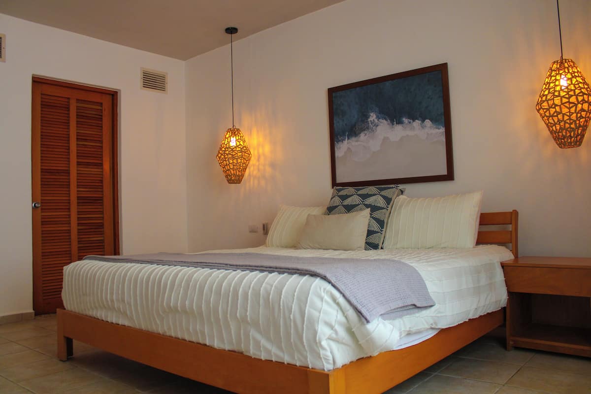 Quarto com cama de madeira, mesa de cabeceira, duas luminárias na parede e um quadro emoldurado.