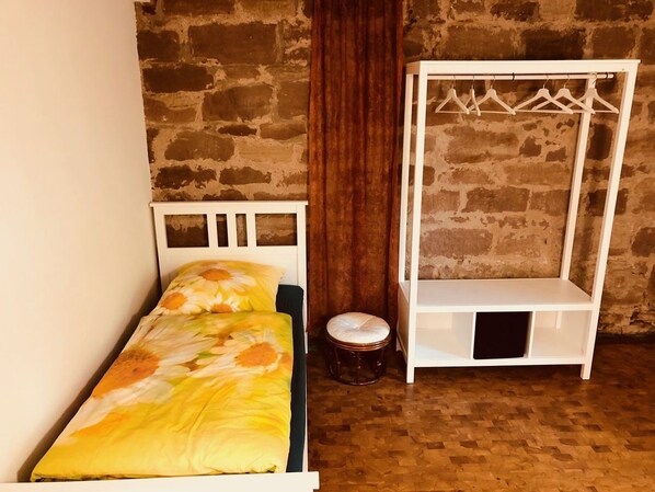 A bed with a floral bedspread, a white wardrobe with a hanging rack, and a wooden stool.