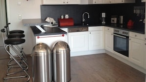 A modern kitchen with white cabinets, a black countertop, stainless steel trash bins, and a coffee machine. - MANUFAKTUR-Ferienwohnungen im Eichsfeld (Niederorschel)