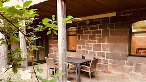 An outdoor patio with a stone wall, a wooden table, and wicker chairs. - MANUFAKTUR-Ferienwohnungen im Eichsfeld (Niederorschel)
