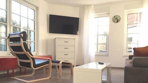 A modern living room with a TV, a sofa, a chair, a small table, and a cabinet. - MANUFAKTUR-Ferienwohnungen im Eichsfeld (Niederorschel)
