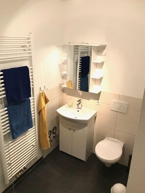Ein kleines Badezimmer mit einem weißen Waschbecken, einem Spiegel, einer Toilette und einem Handtuchhalter.