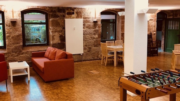 A cozy room with a wooden floor, a red sofa, a white table, and a foosball table. - MANUFAKTUR-Ferienwohnungen im Eichsfeld (Niederorschel)