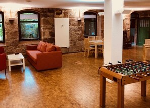 A cozy room with a wooden floor, a red sofa, a white table, and a foosball table. - MANUFAKTUR-Ferienwohnungen im Eichsfeld (Niederorschel)