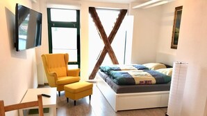A bedroom with a bed, a yellow armchair, a small table, and a TV mounted on the wall. - MANUFAKTUR-Ferienwohnungen im Eichsfeld (Niederorschel)