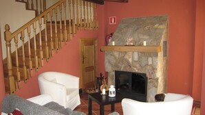 Un salon avec une cheminée en pierre, des canapés blancs, un escalier en bois et un mur rouge.