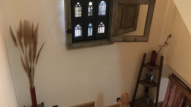Un escalier en bois, agrémenté d’une étagère rustique fixée au mur, sur laquelle repose un objet décoratif, et une petite fenêtre ornée de vitraux.