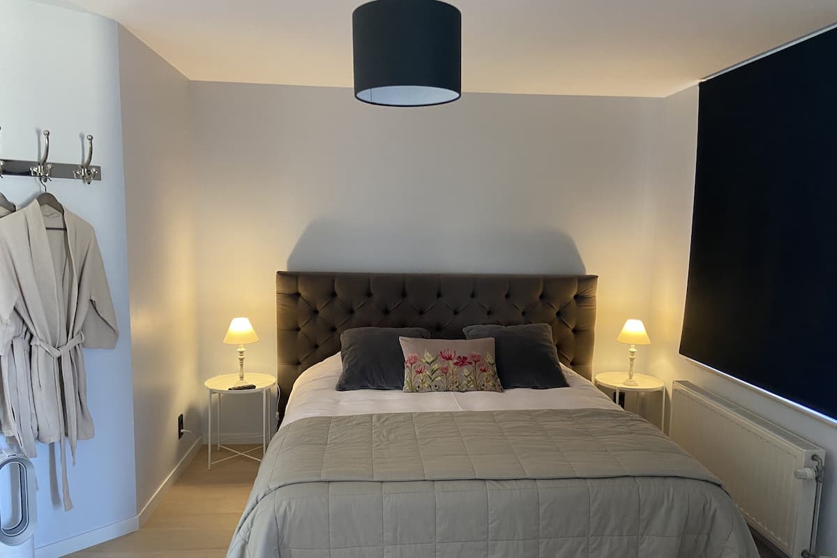 A bedroom with a large bed, two bedside lamps, a robe hanging on the wall, and a radiator.