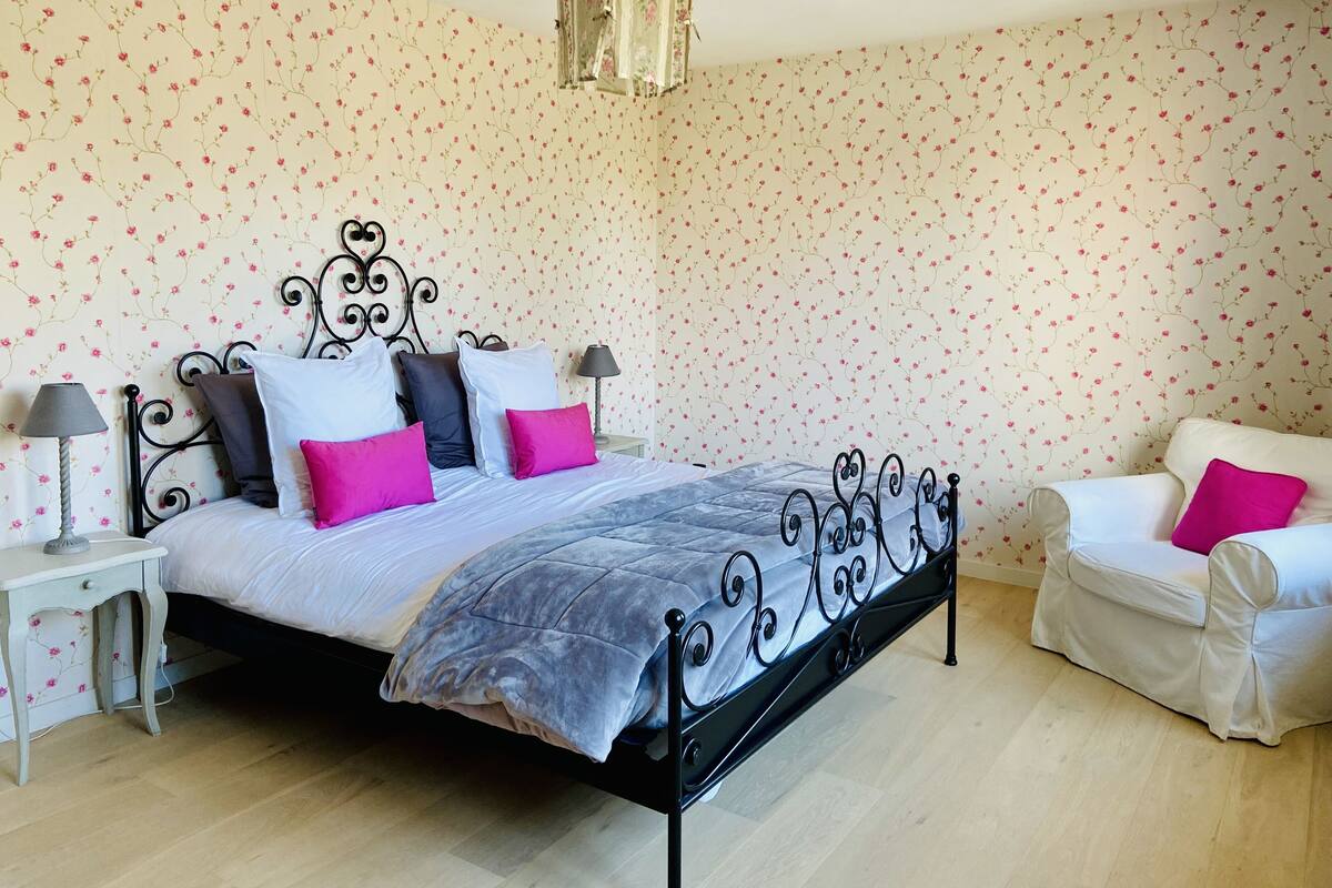 A bedroom with a bed, bedside tables, a chair, and floral wallpaper.
