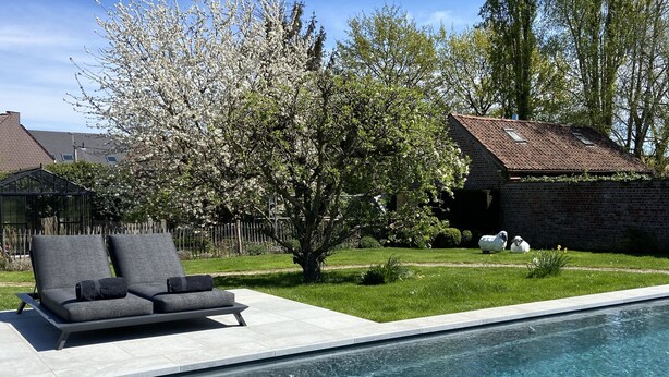 A swimming pool with a modern lounge area and a brick building in the background. - B&B Aline Florentine (Kortenberg)