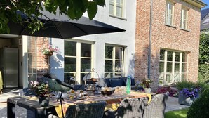 A patio area with wicker furniture, a table with a yellow tablecloth, and a hanging flower basket. - B&B Aline Florentine (Kortenberg)