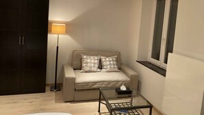 Una sala de estar con un sofá, una lámpara de pie, una mesa de centro de vidrio y una ventana con persianas.